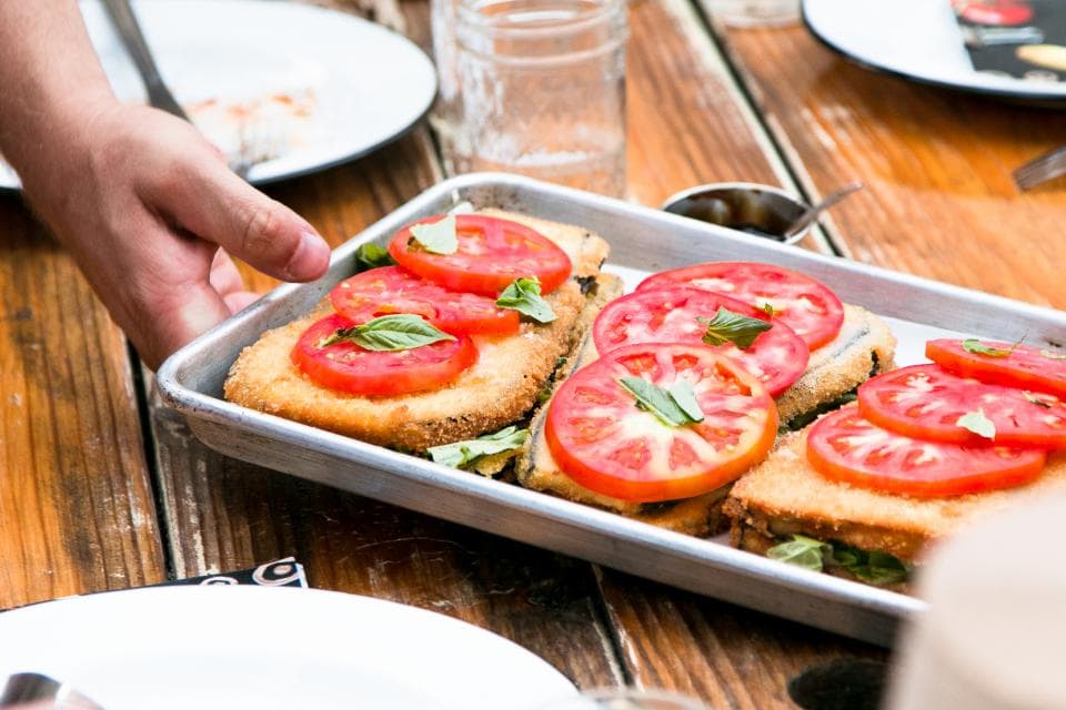 Une main dépose sur la table un plateau de plats prêts à servir.